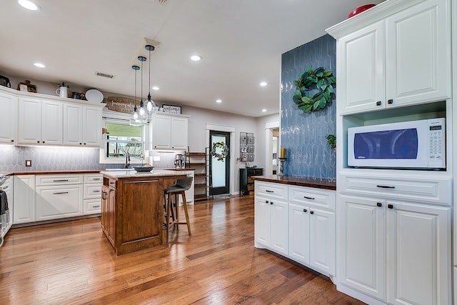 kitchen featuring white microwave, visible vents, backsplash, and light wood-style floors