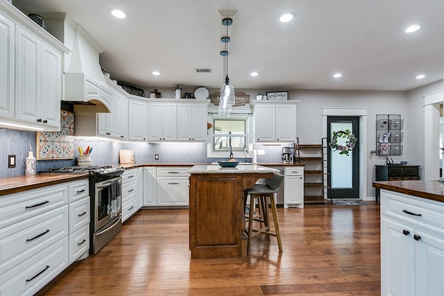 kitchen featuring stainless steel range with gas cooktop, dark wood-style flooring, premium range hood, and white cabinetry