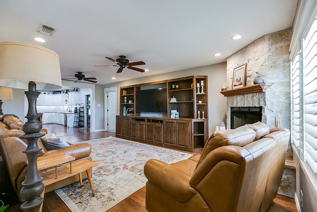 living room with recessed lighting, visible vents, ceiling fan, a stone fireplace, and wood finished floors