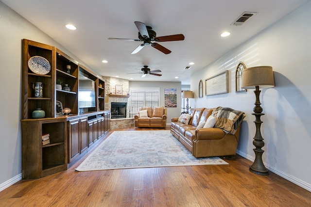 living room featuring recessed lighting, a fireplace, wood finished floors, visible vents, and baseboards