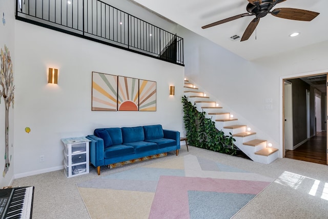 carpeted living area featuring baseboards, visible vents, a ceiling fan, stairway, and a high ceiling