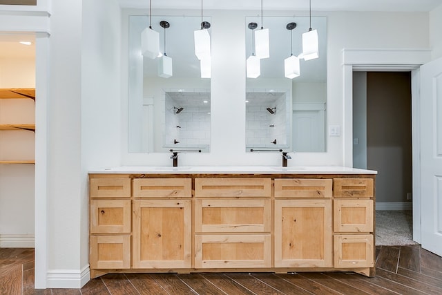 full bath with baseboards, a walk in closet, a tile shower, wood finish floors, and a sink