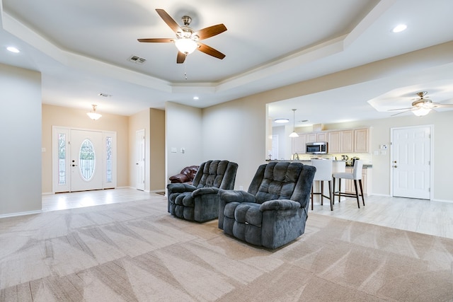 living room with light carpet, a tray ceiling, visible vents, and baseboards