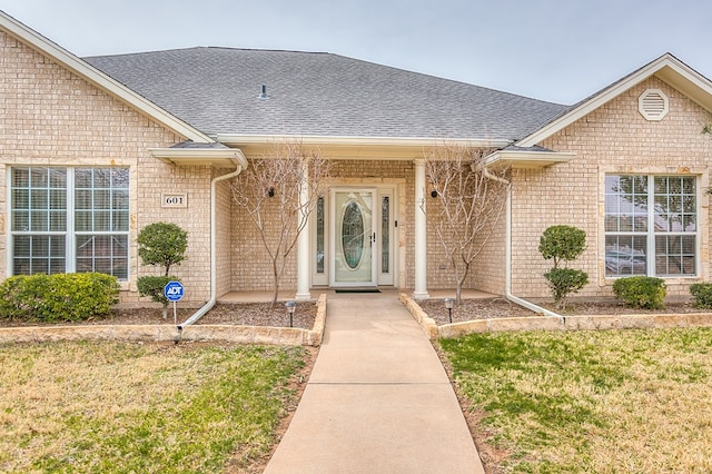 entrance to property with a yard, a shingled roof, and brick siding