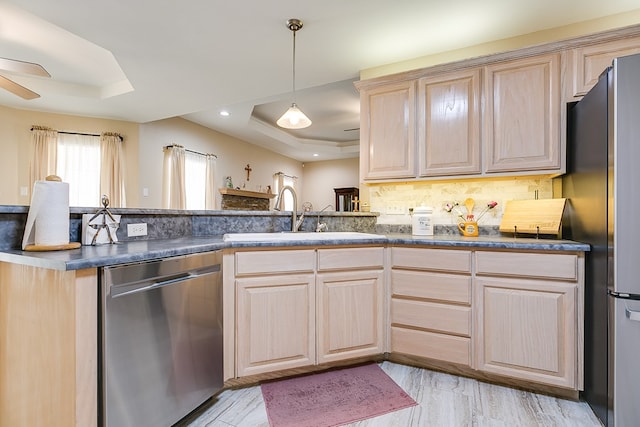 kitchen with ceiling fan, a sink, appliances with stainless steel finishes, light brown cabinetry, and a tray ceiling