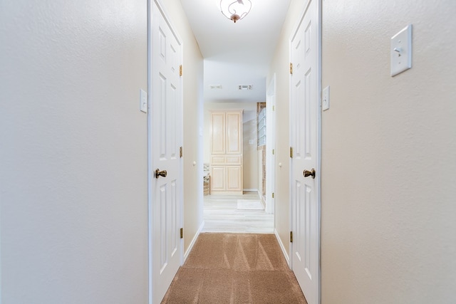 hall with visible vents, baseboards, and light colored carpet