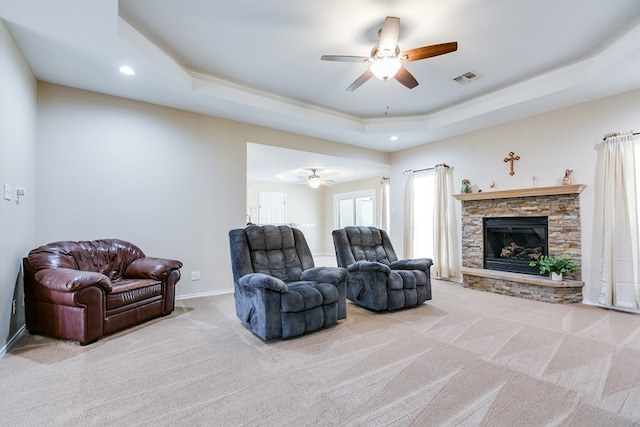 living area with carpet floors, a tray ceiling, visible vents, and a stone fireplace