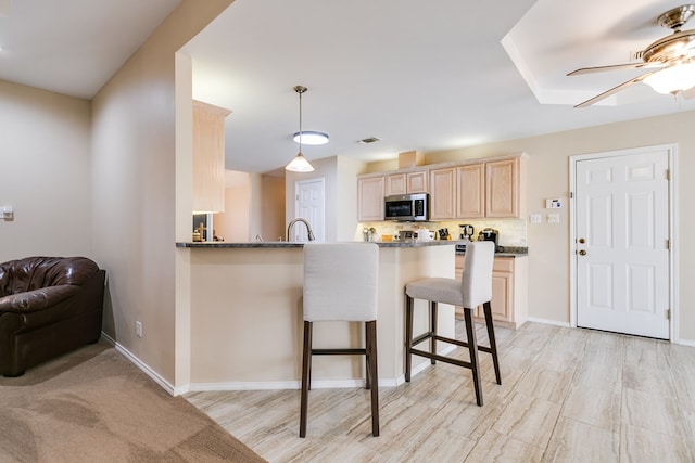 kitchen featuring a breakfast bar area, light brown cabinets, a peninsula, tasteful backsplash, and stainless steel microwave