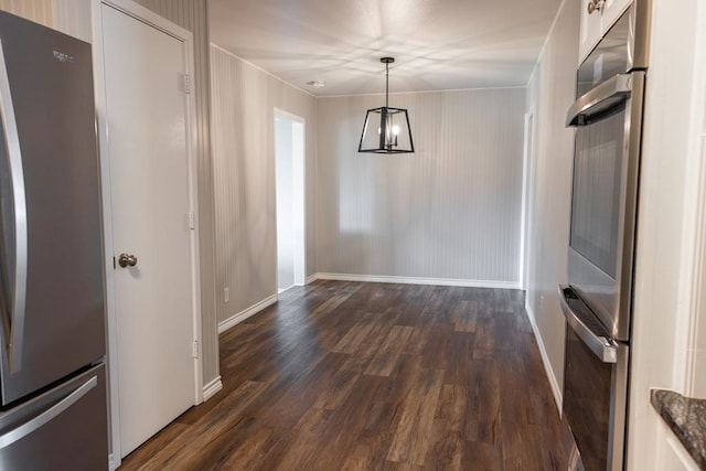 unfurnished dining area featuring dark wood-type flooring, a notable chandelier, baseboards, and ornamental molding
