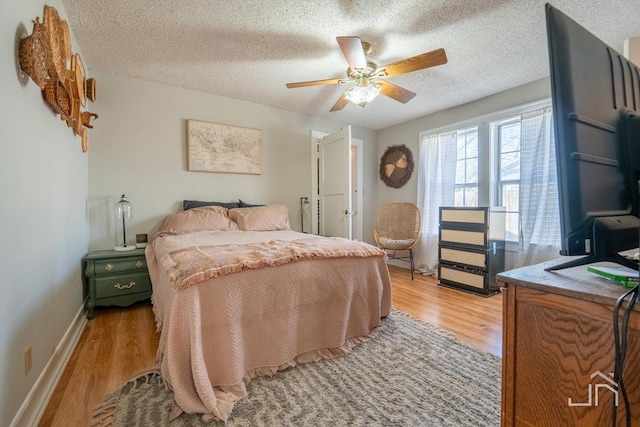 bedroom with baseboards, a textured ceiling, light wood-style flooring, and a ceiling fan