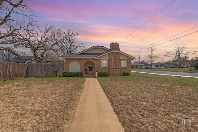 view of front of house featuring brick siding, a chimney, a yard, and fence