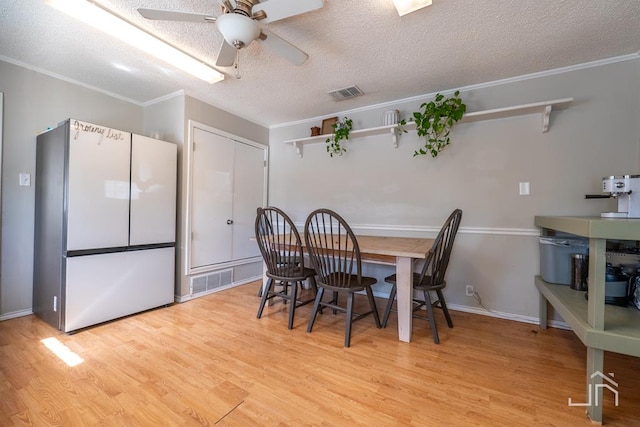 dining area with a textured ceiling, ornamental molding, visible vents, and light wood-type flooring