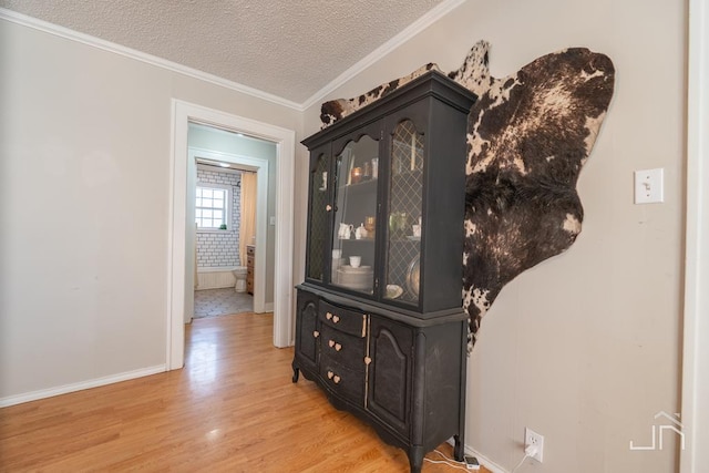 hallway featuring baseboards, a textured ceiling, light wood-style flooring, and ornamental molding