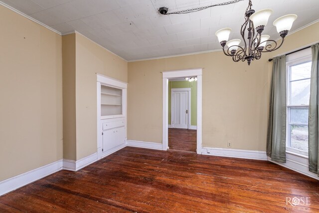 empty room with crown molding, dark hardwood / wood-style floors, and an inviting chandelier