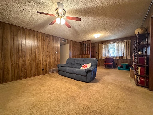 carpeted living room with ceiling fan, wooden walls, and a textured ceiling