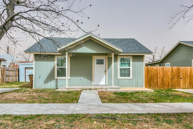 bungalow featuring a front yard, roof with shingles, and fence