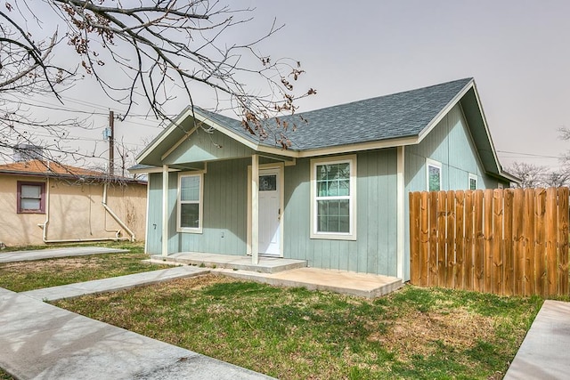 bungalow-style home featuring roof with shingles, a front yard, and fence