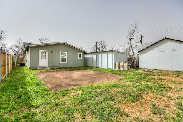 back of house featuring central air condition unit, fence, a lawn, and an outbuilding