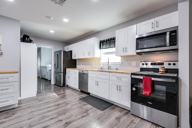 kitchen with stainless steel appliances, a sink, white cabinets, and washer and dryer