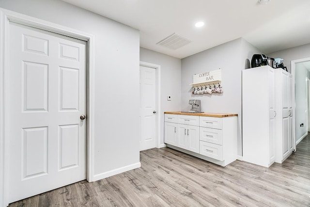 kitchen with light wood-style floors, white cabinets, visible vents, and wood counters