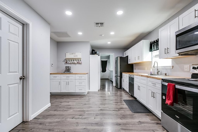 kitchen with appliances with stainless steel finishes, butcher block countertops, a sink, and white cabinets