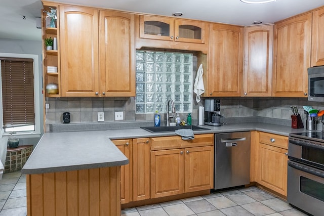 kitchen featuring appliances with stainless steel finishes, a sink, light tile patterned floors, backsplash, and glass insert cabinets