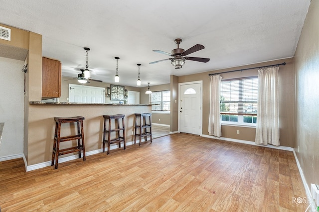interior space with light wood-type flooring, a kitchen breakfast bar, baseboards, and a ceiling fan