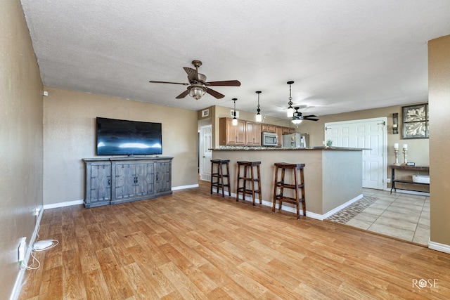 living room with visible vents, ceiling fan, light wood finished floors, and baseboards