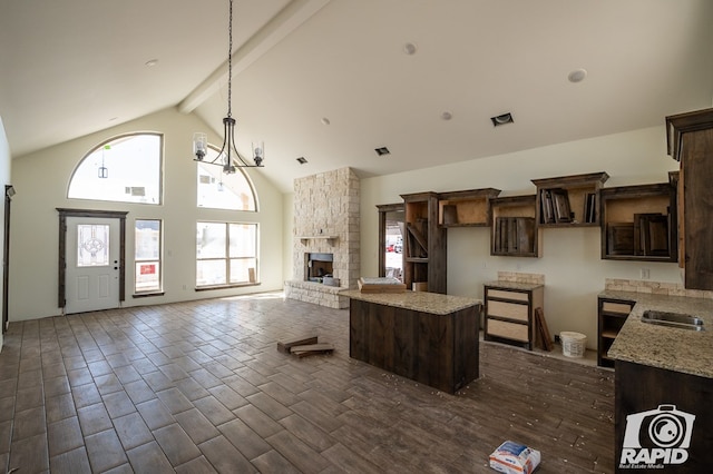 kitchen featuring dark wood-style floors, a center island, beam ceiling, dark brown cabinetry, and a stone fireplace