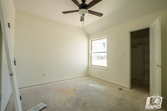 unfurnished bedroom with a closet, a spacious closet, a ceiling fan, vaulted ceiling, and concrete flooring