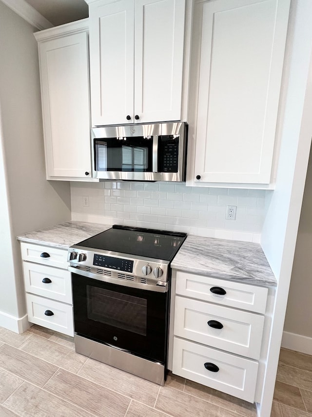 kitchen featuring tasteful backsplash, light stone countertops, white cabinets, and appliances with stainless steel finishes