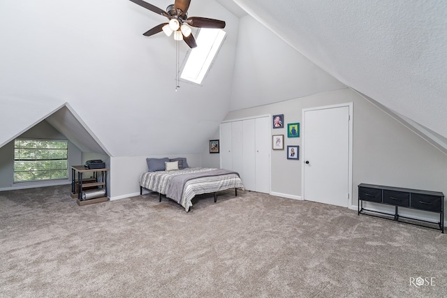 bedroom featuring carpet, vaulted ceiling with skylight, a textured ceiling, and ceiling fan