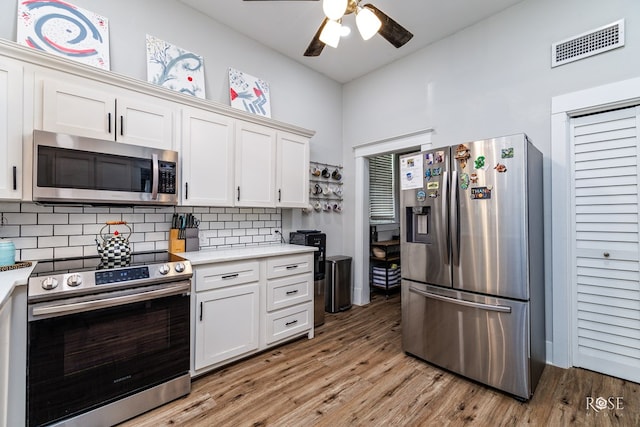 kitchen featuring appliances with stainless steel finishes, white cabinets, decorative backsplash, ceiling fan, and light hardwood / wood-style floors