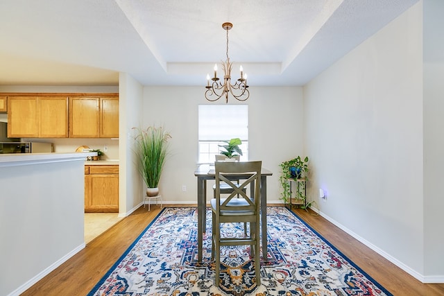 4413 Pinon Ridge Dr, San Angelo, TX 76904 - dining space featuring light wood-style flooring, a chandelier, a raised ceiling, and baseboards