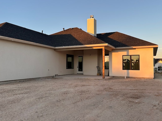 rear view of house featuring stucco siding, a patio, a chimney, and a shingled roof