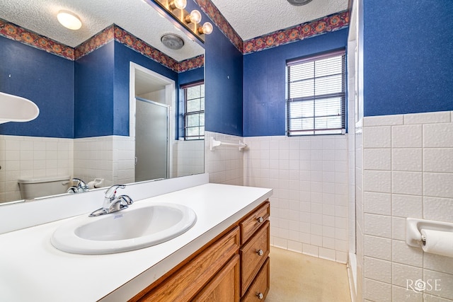 3222 Oak Mountain Trl, San Angelo, TX 76904 - full bathroom featuring tile walls, a textured ceiling, an enclosed shower, vanity, and wainscoting