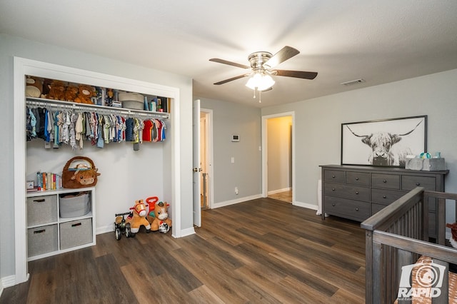 bedroom featuring a nursery area, ceiling fan, dark wood-type flooring, and a closet