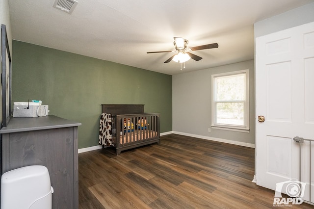 bedroom with dark hardwood / wood-style flooring, a crib, and ceiling fan