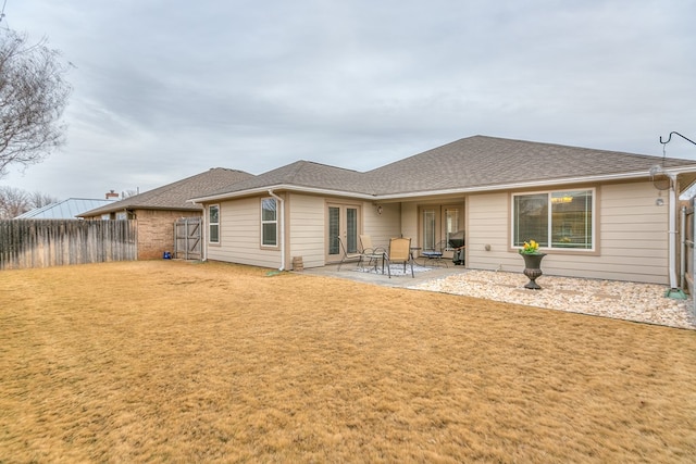 rear view of property featuring a shingled roof, a lawn, fence, french doors, and a patio area