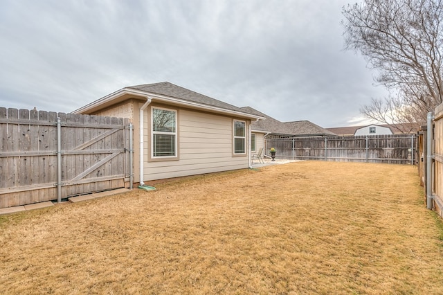 rear view of property with a shingled roof, a gate, a fenced backyard, and a lawn