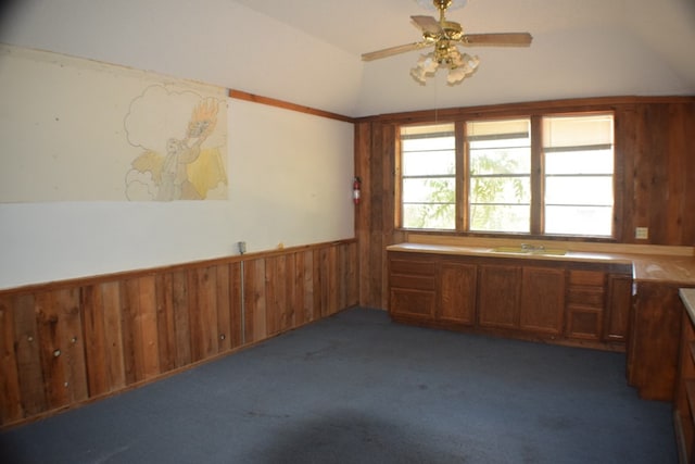 carpeted spare room featuring ceiling fan, vaulted ceiling, and wood walls