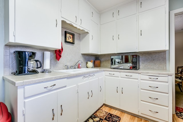 kitchen featuring light wood-type flooring, sink, tasteful backsplash, and white cabinets