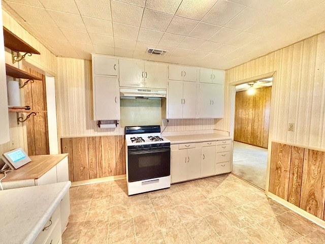 kitchen featuring white gas range, white cabinets, and wooden walls