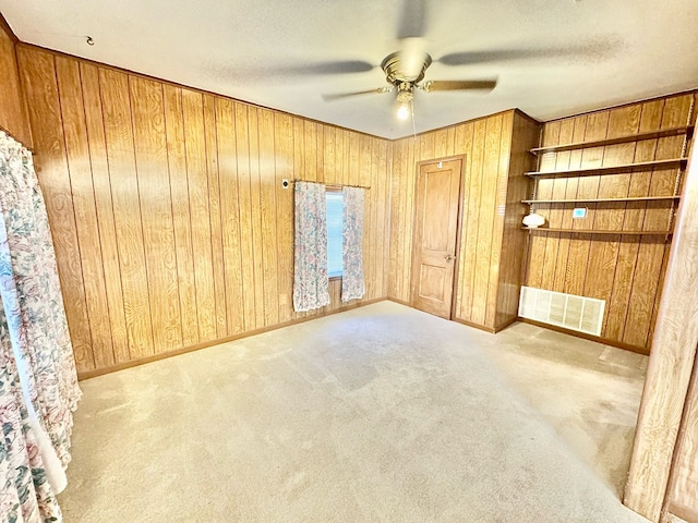 unfurnished bedroom with ceiling fan, a textured ceiling, light carpet, and wood walls