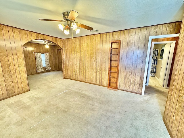 carpeted empty room featuring ceiling fan, wooden walls, and a textured ceiling