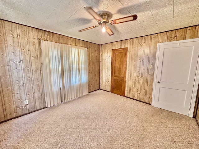 unfurnished bedroom featuring carpet, wooden walls, and ceiling fan