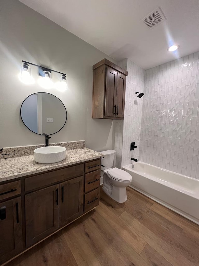 full bathroom with hardwood / wood-style flooring, tiled shower / bath, vanity, and toilet