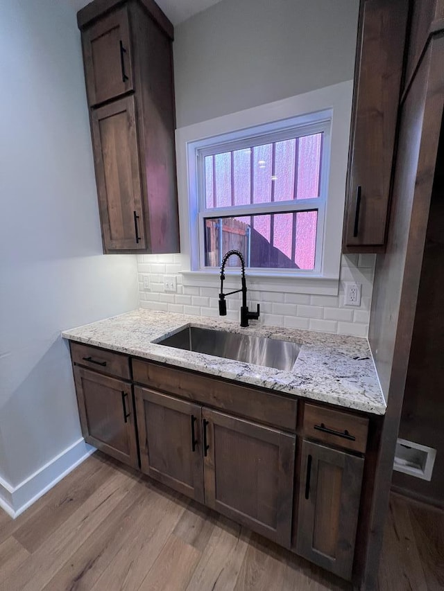 kitchen featuring sink, backsplash, light stone counters, and light wood-type flooring