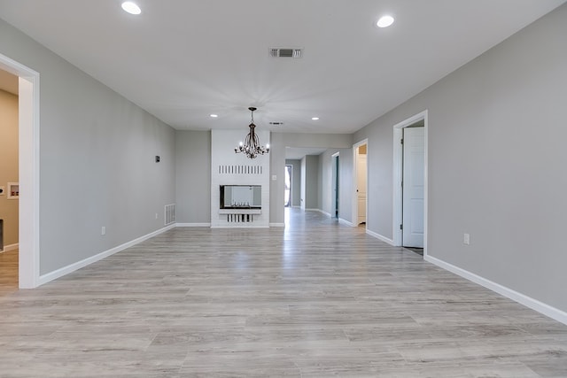 unfurnished living room with light hardwood / wood-style floors, a brick fireplace, and a notable chandelier