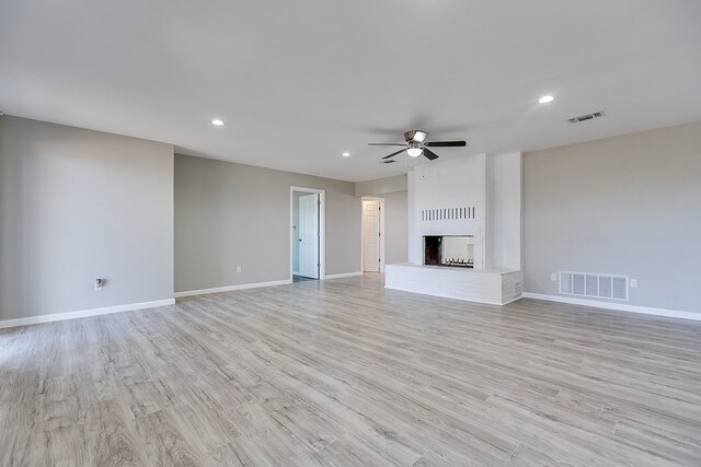 unfurnished living room with ceiling fan, a brick fireplace, and light wood-type flooring